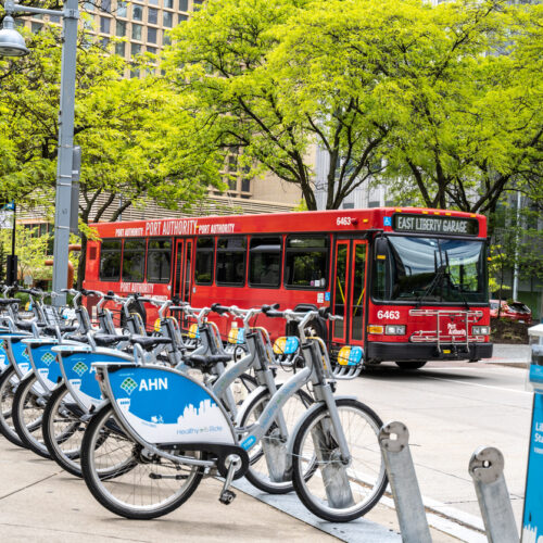 Ride bike share station with red public bus passing in the background.