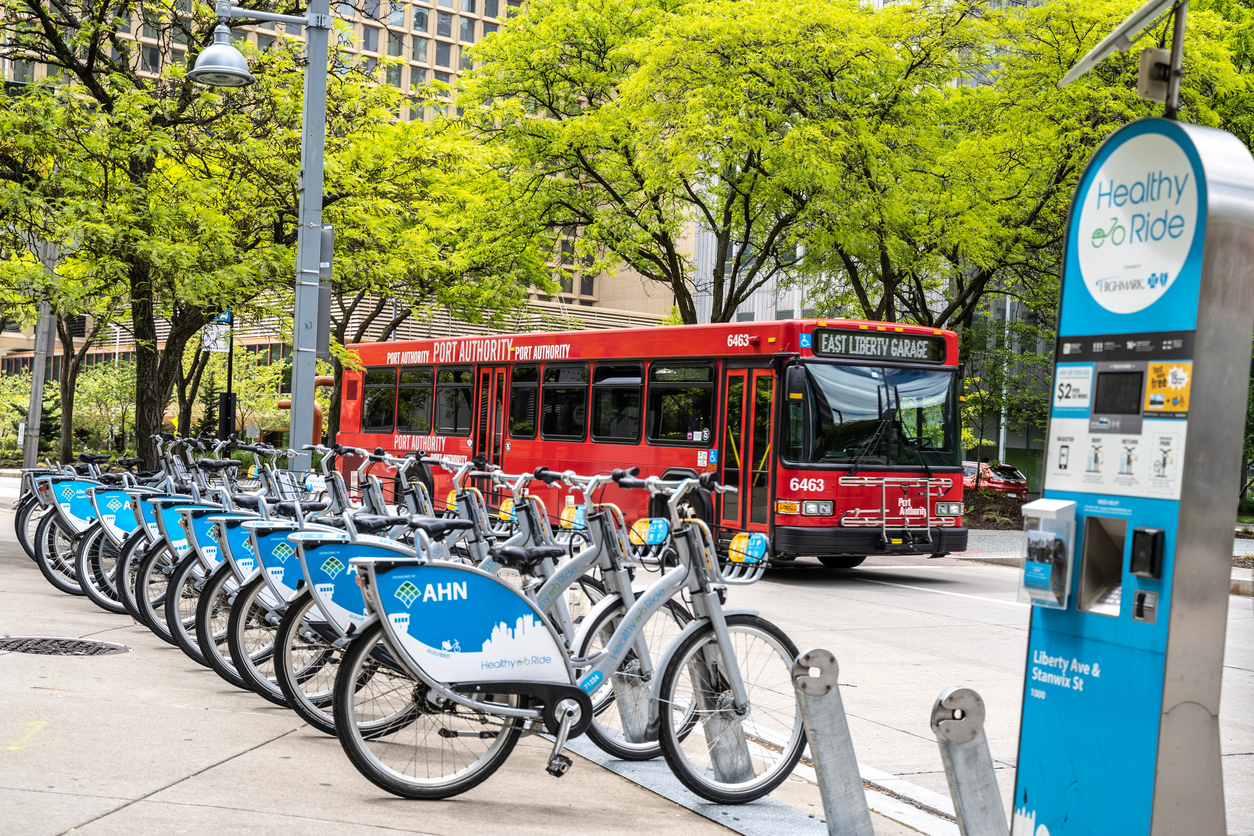 Ride bike share station with red public bus passing in the background.