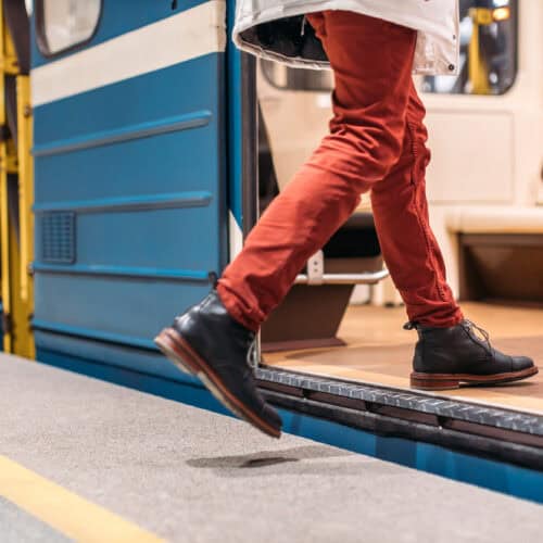 Person in black shoes, burgundy pants and white jacket runs into a subway train.