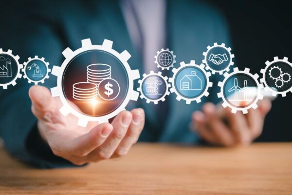 Hand holding a gear with money coins, surrounded by icons for industry, construction, energy, and global collaboration